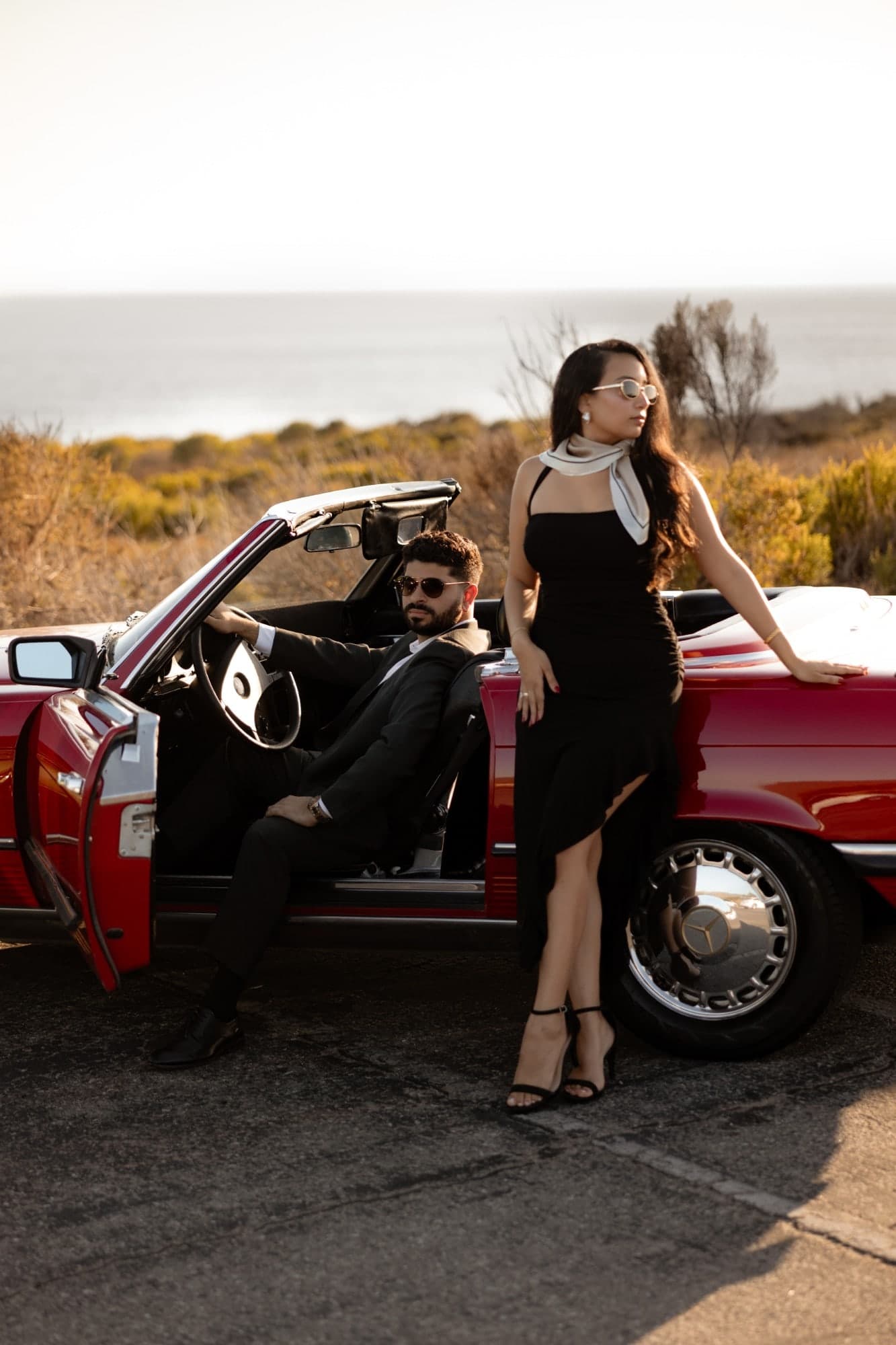David and Joy with a vintage Mercedes convertible on a coastal bluff, the ocean behind them